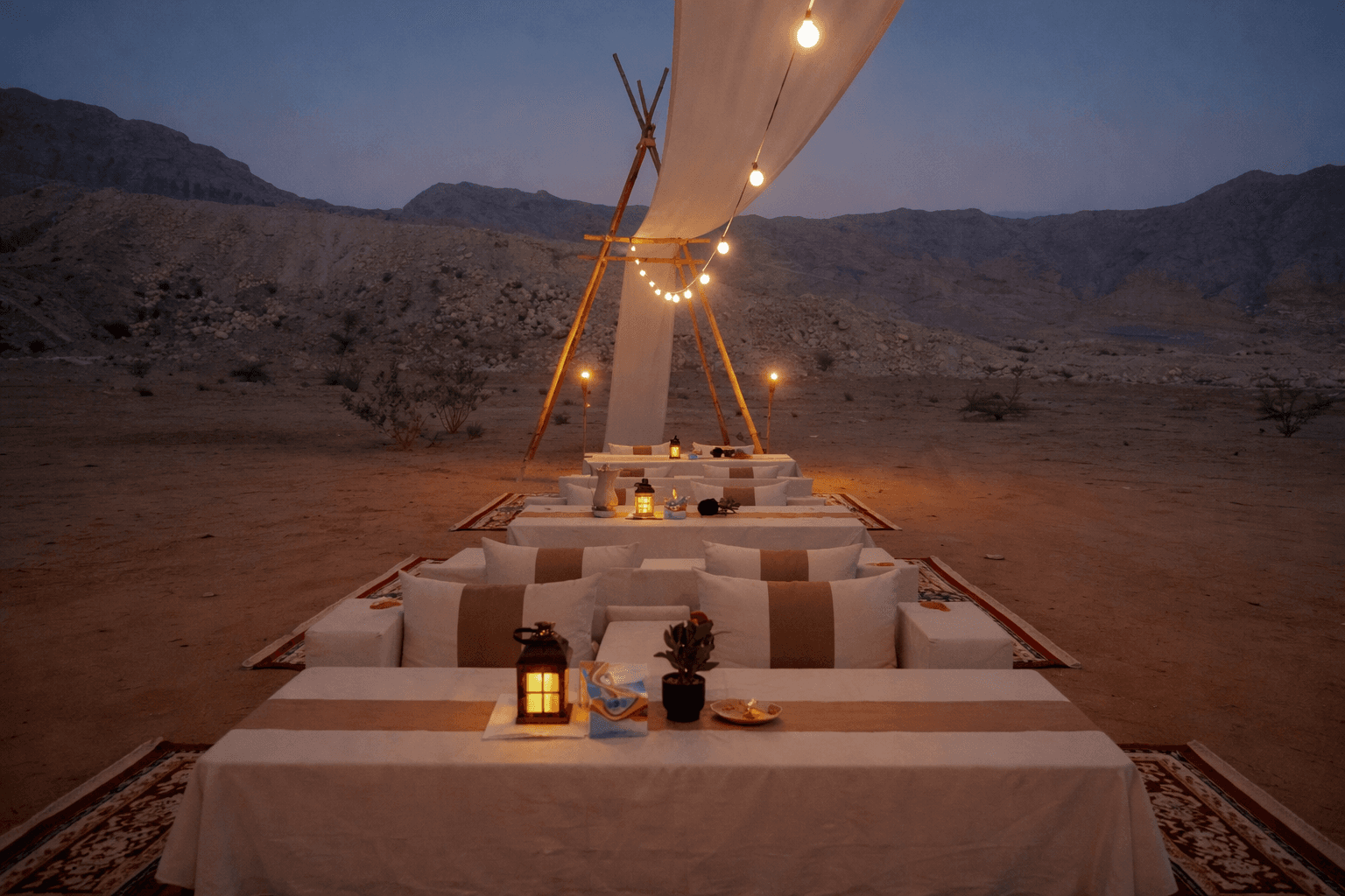 Shared desert dining tables under lights at Zerzura Mleiha desert camp