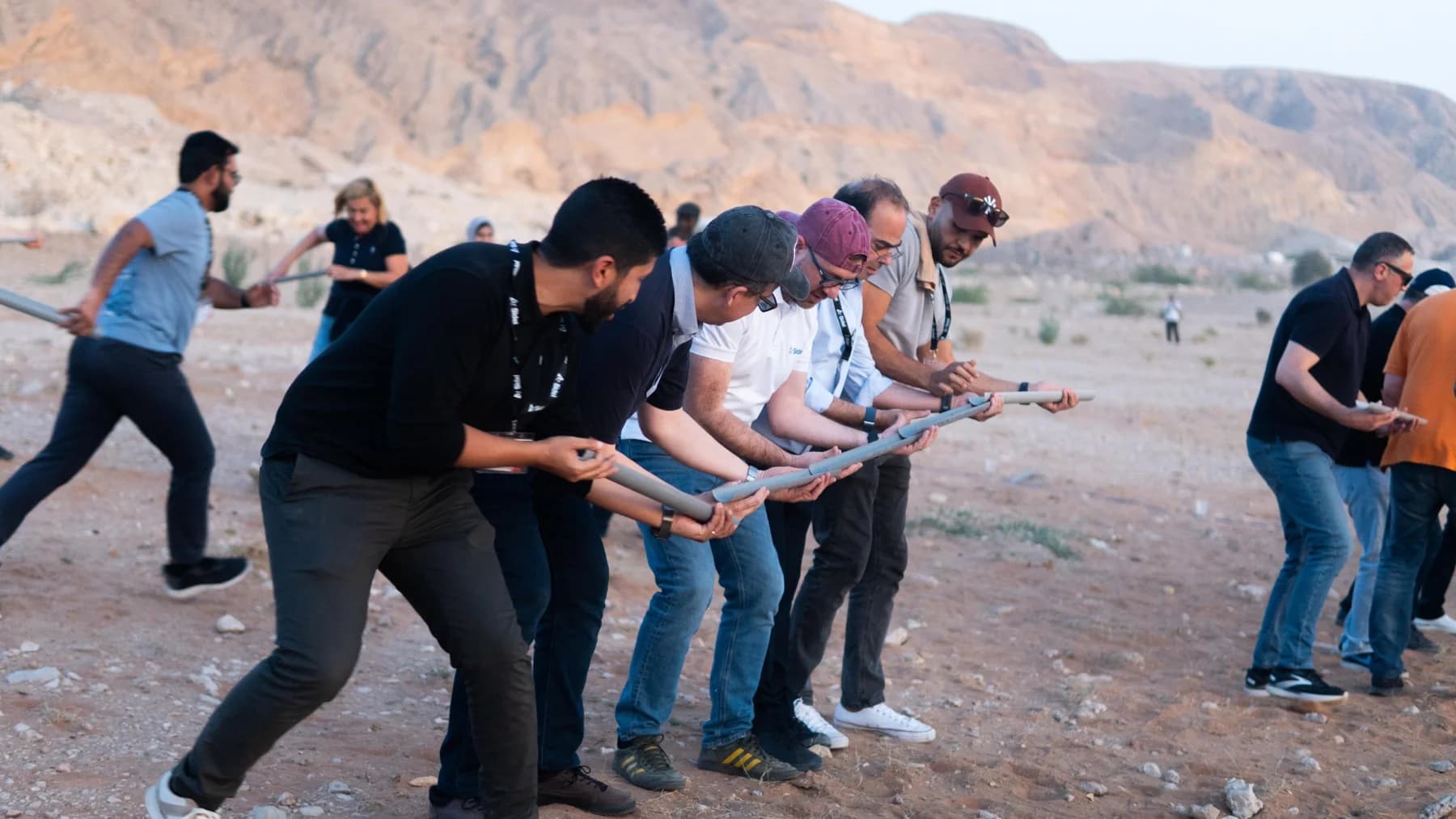 Teams coordinating a ball relay using sections of pipe in the desert