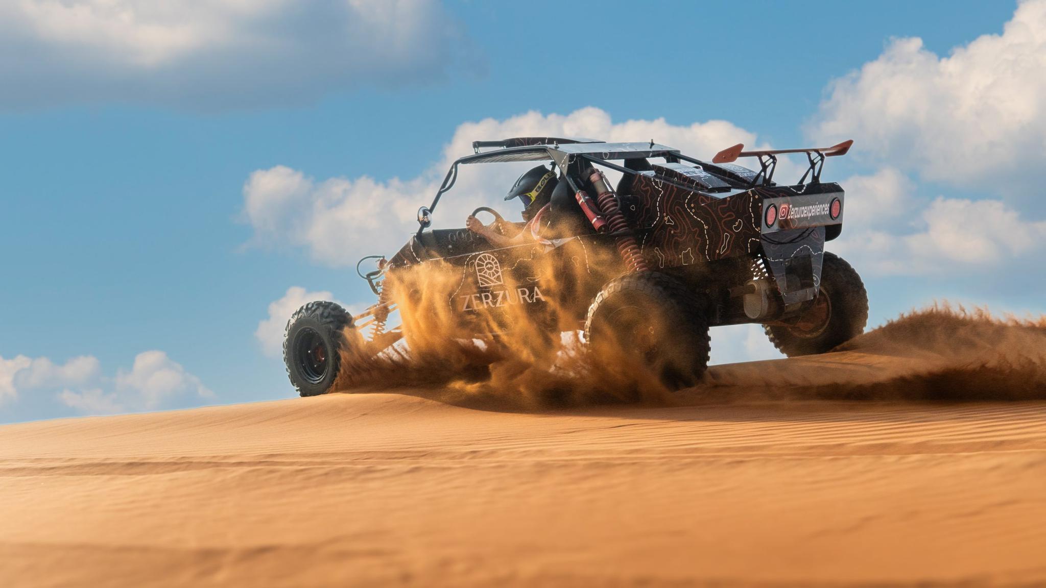 Powerful dune buggy kicking up sand during an off-road ride in Dubai desert, branded with Zerzura Experiences logo under clear blue skies.