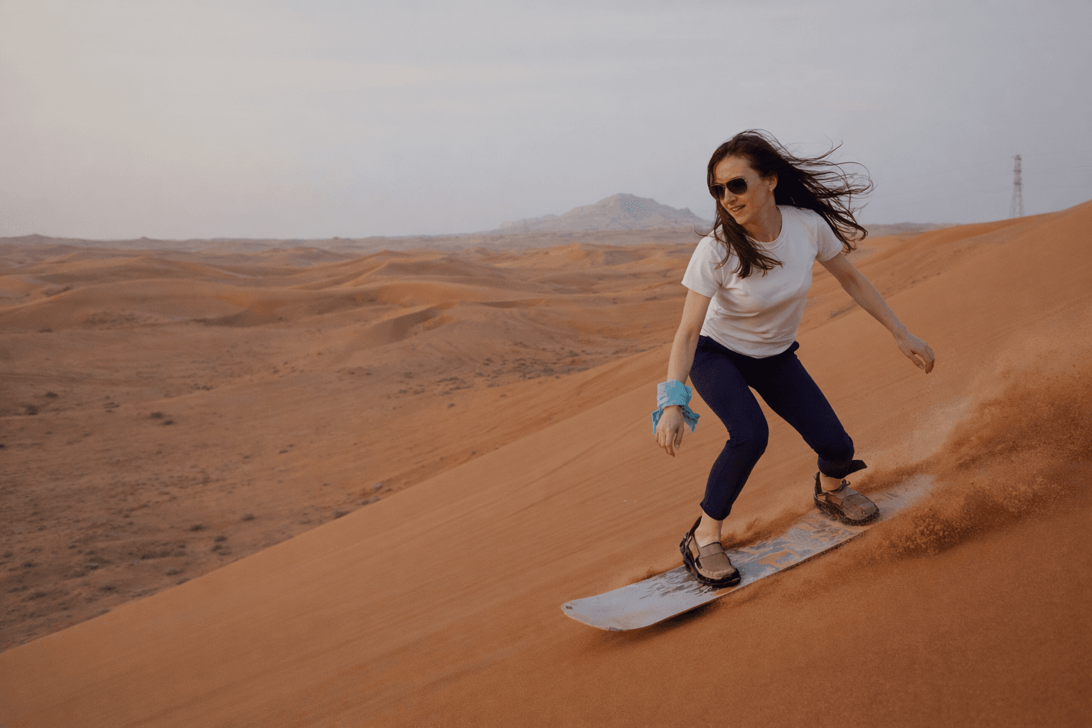 Guest sandboarding down desert dune in Mleiha near Zerzura camp