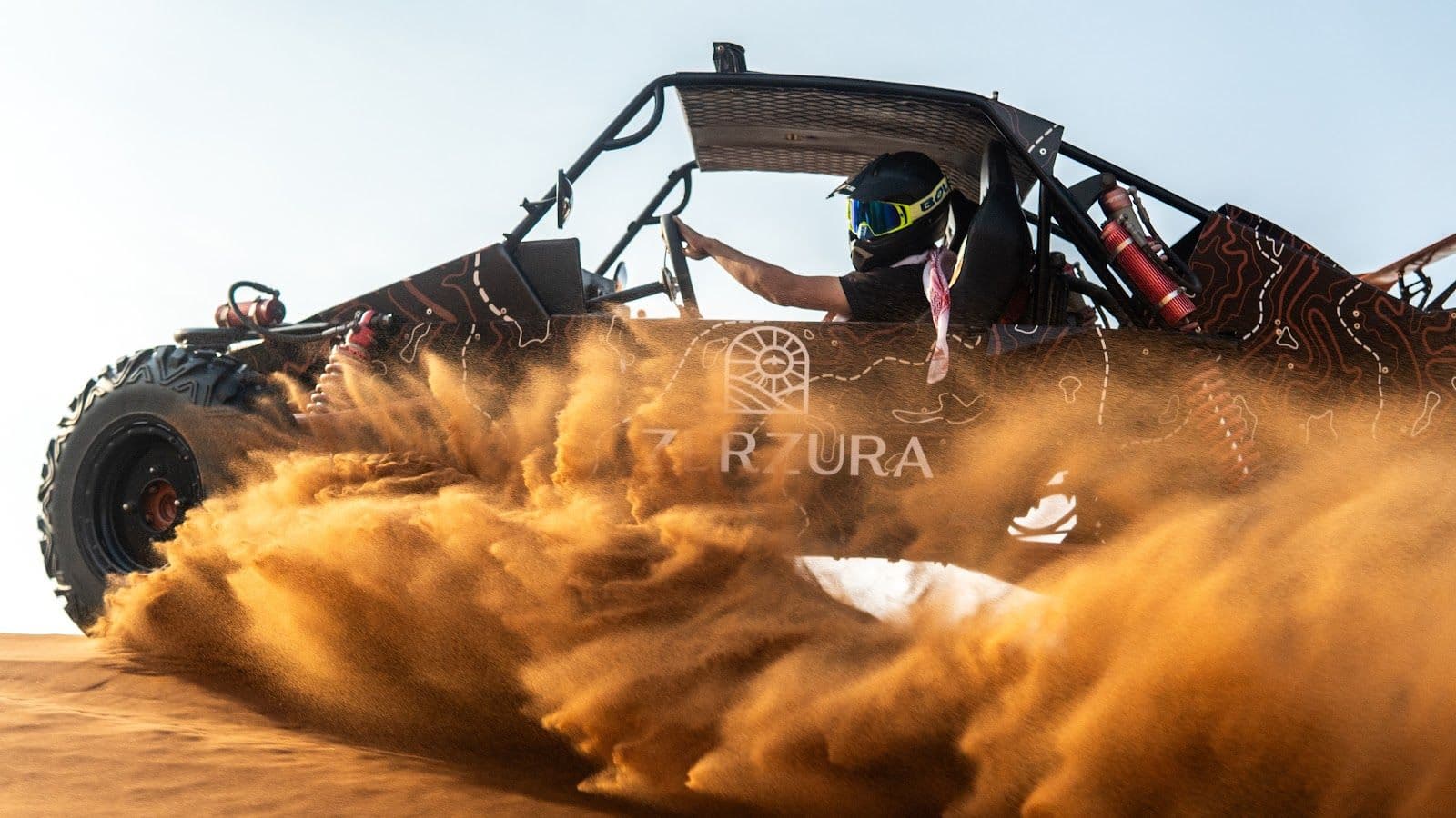 Helmeted driver in a Zerzura dune buggy kicking up sand in Mleiha